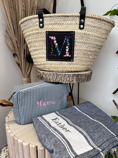 Bolso capazo con inicial M sobre cuero negro, acompañado de neceser y toalla personalizada

