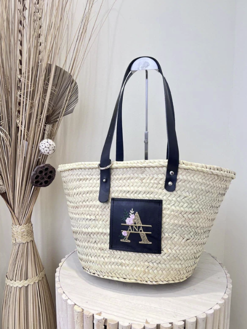 Capazo de rafia con asas negras y bordado floral personalizado sobre parche de cuero negro


