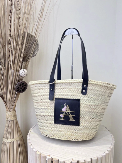 Capazo de rafia con asas negras y bordado floral personalizado sobre parche de cuero negro


