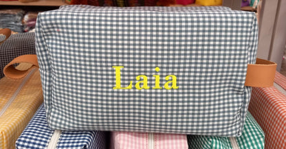 Neceser de cuadros Vichy gris personalizado con el nombre "Laia" bordado en amarillo y asa de piel