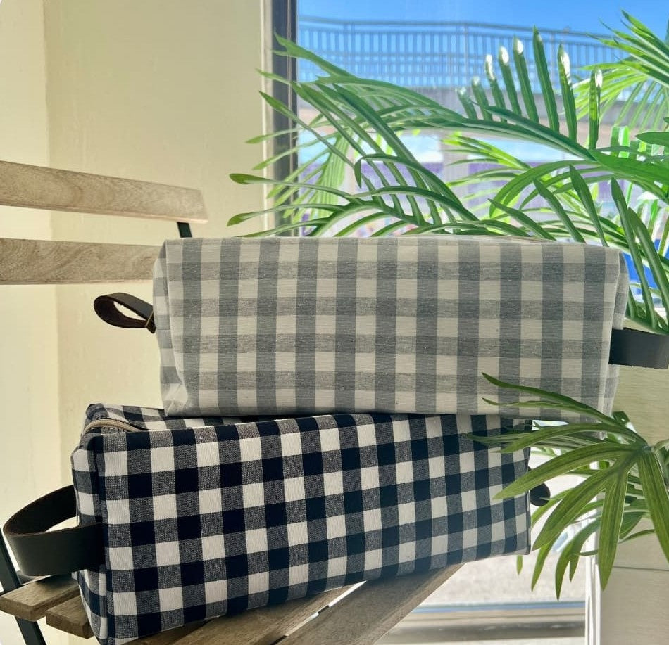 Neceser grande con estampado vichy en tonos blanco y gris sobre banco de madera

