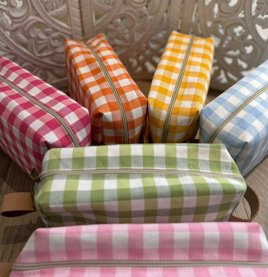 Neceseres Vichy en rosa, azul cielo, naranja, verde y amarillo dispuestos sobre superficie decorativa