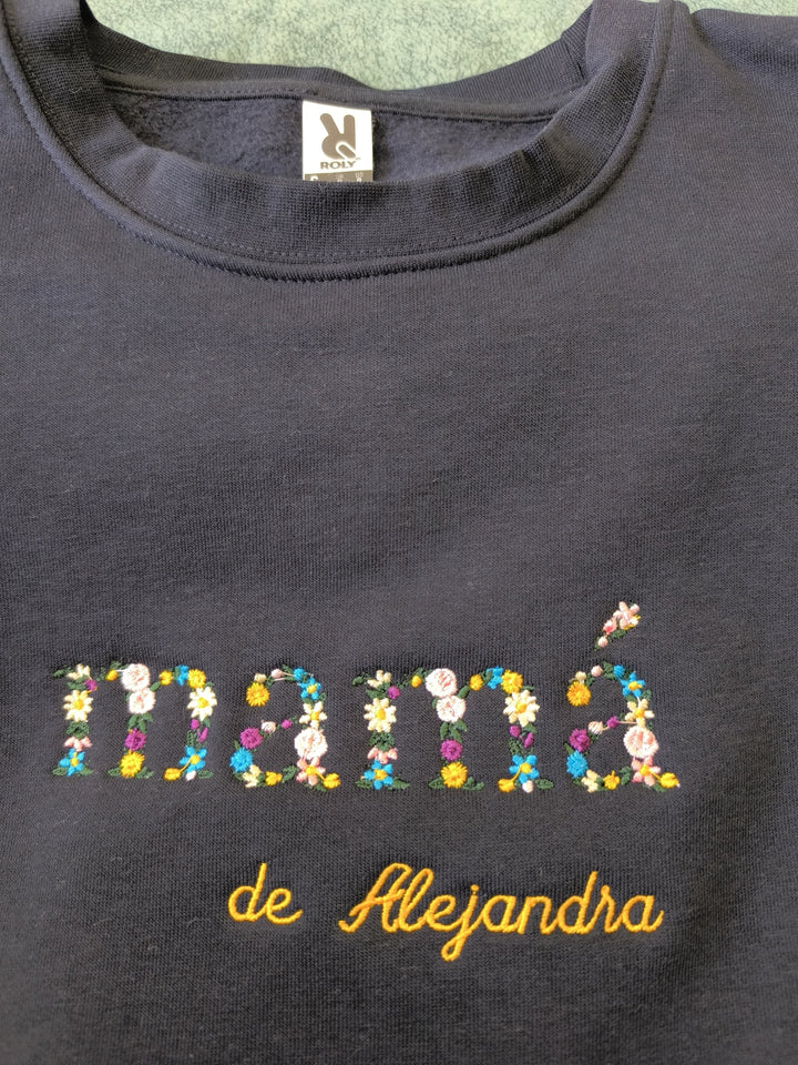 Sudadera negra con la palabra “mamá” bordada en flores junto a nombres personalizados, diseño delicado y artesanal