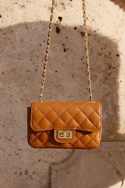 Bolso Accardi de piel italiana colgado con cadena dorada en fondo natural

