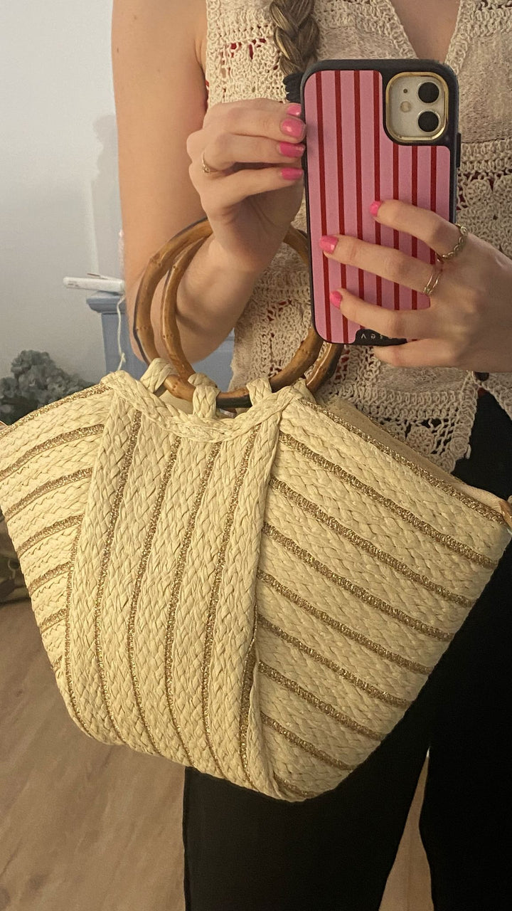 Bolso capazo Kuta con asas de madera sobre fondo de mar, el complemento boho chic perfecto para el verano.

