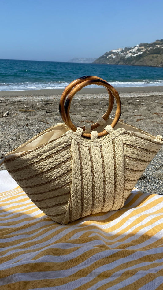 Capazo Kuta en la playa con toalla de rayas y accesorios de verano, ideal para tus días de sol y estilo.

